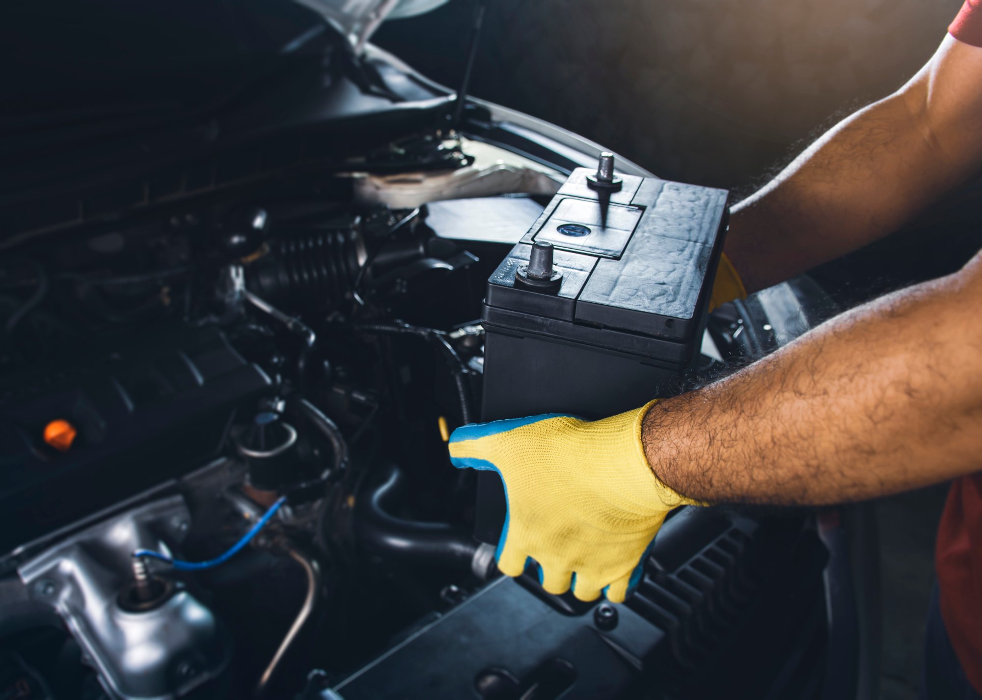 Mechanic in yellow gloves checking car battery under open hood