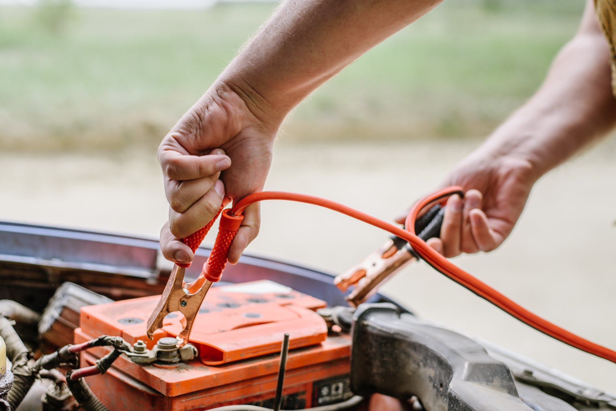 Person connecting jumper cables to car battery terminal during roadside assistance