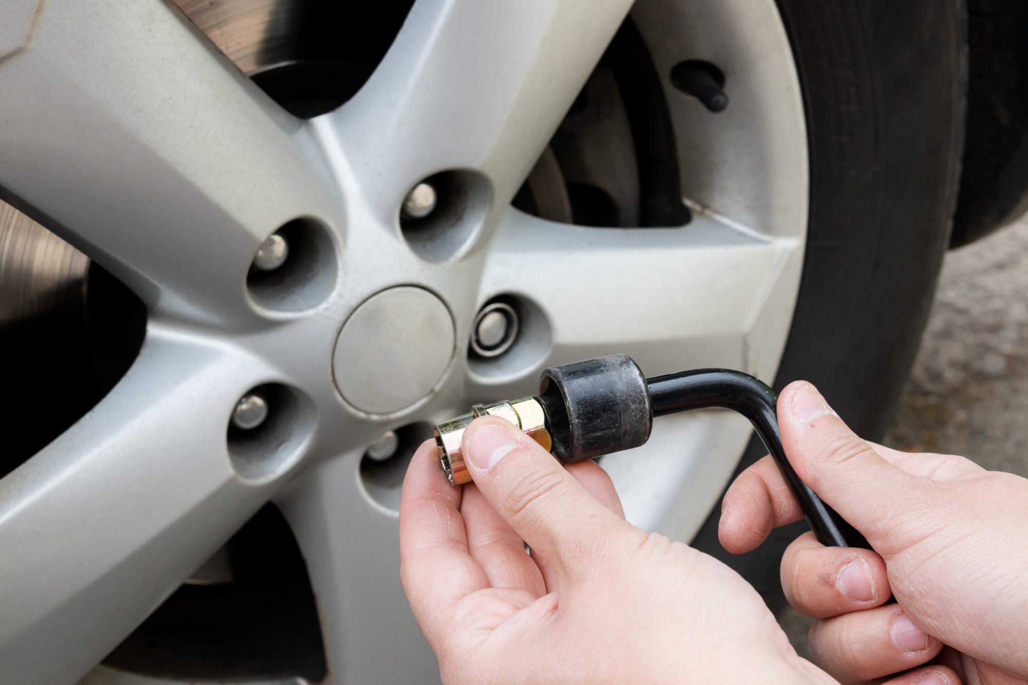 Person holding tire pressure gauge against white alloy wheel