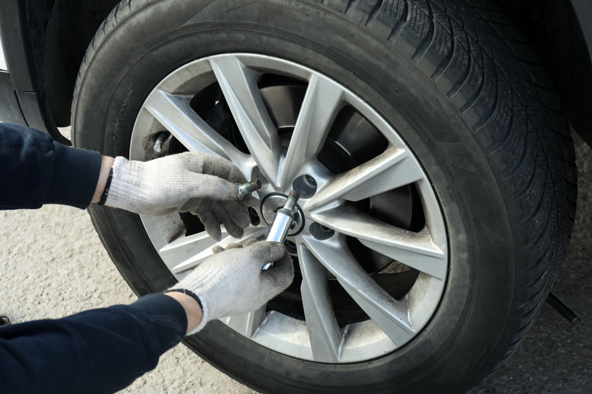 Person in white gloves using a lug wrench to remove a wheel nut from a silver alloy wheel